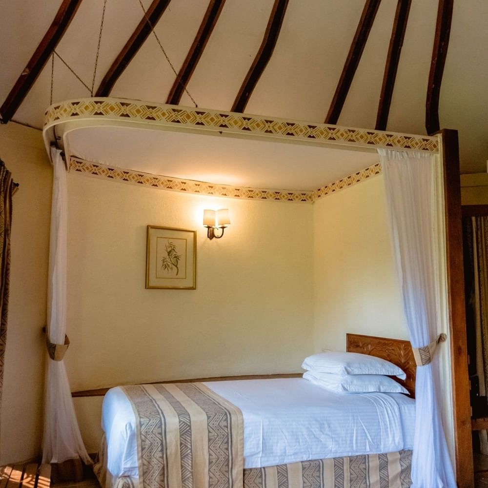 Cozy Standard Triple Room at Arusha Serena Hotel in Arusha with a canopy bed and wooden decor.