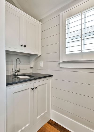 Modern utility space with white cabinets, black countertop, sink, and window shutters by Cottages at Laurel Brooke