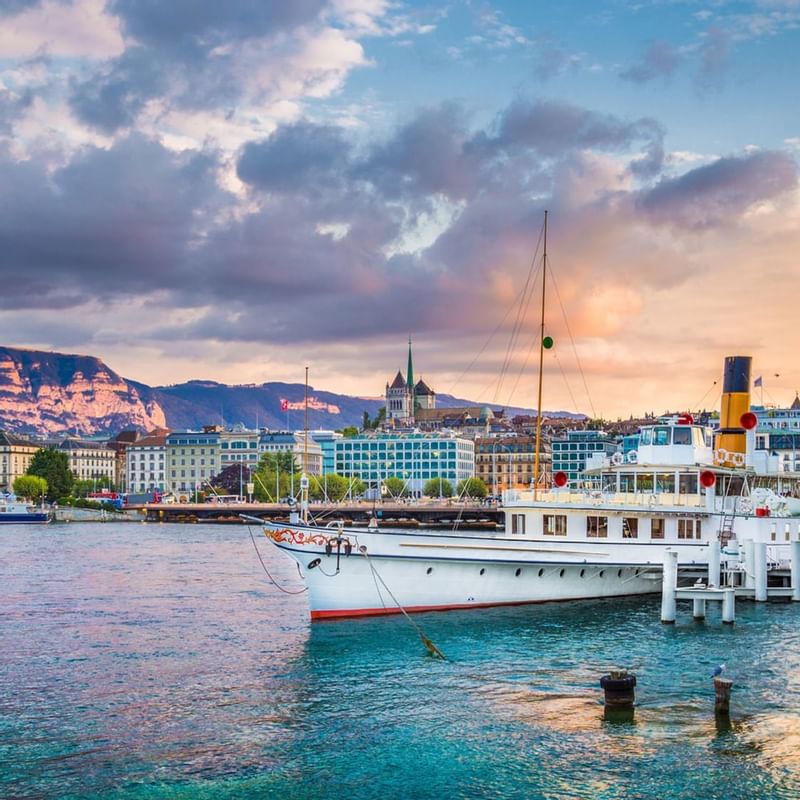 Steamboat docked on Lake Geneva near Warwick Hotels and Resorts, with a cityscape, and mountains