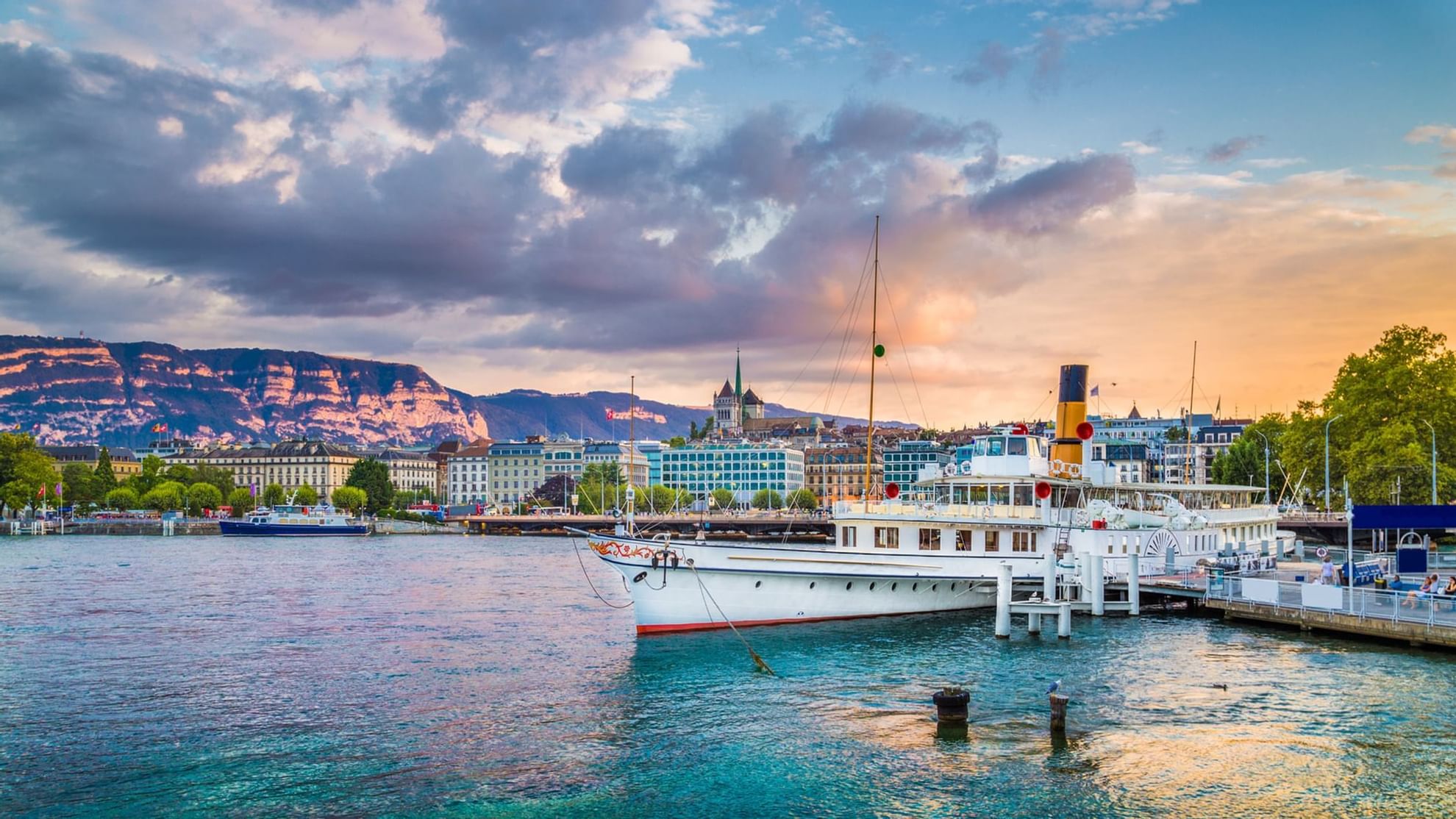 Steamboat docked on Lake Geneva near Warwick Hotels and Resorts, with a cityscape, and mountains
