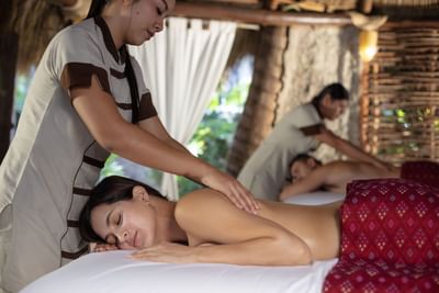 A couple receiving a relaxing outdoor massage from professional therapists under an open-air palapa.