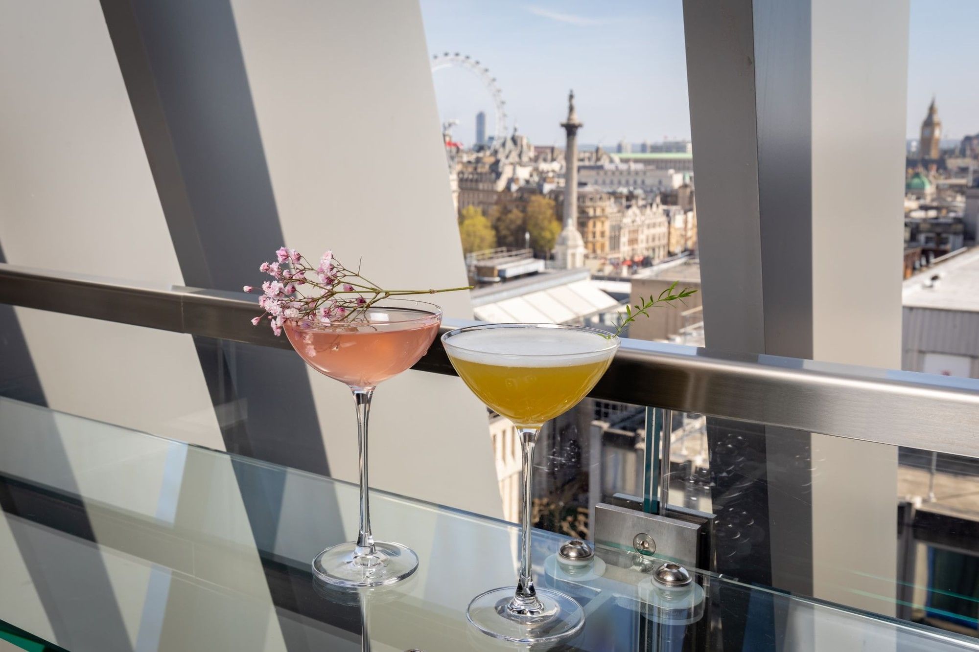 Des cocktails roses et jaunes dégustés sur le rebord vitré d'un balcon donnant sur la silhouette du London Eye, à l'hôtel The Londoner
