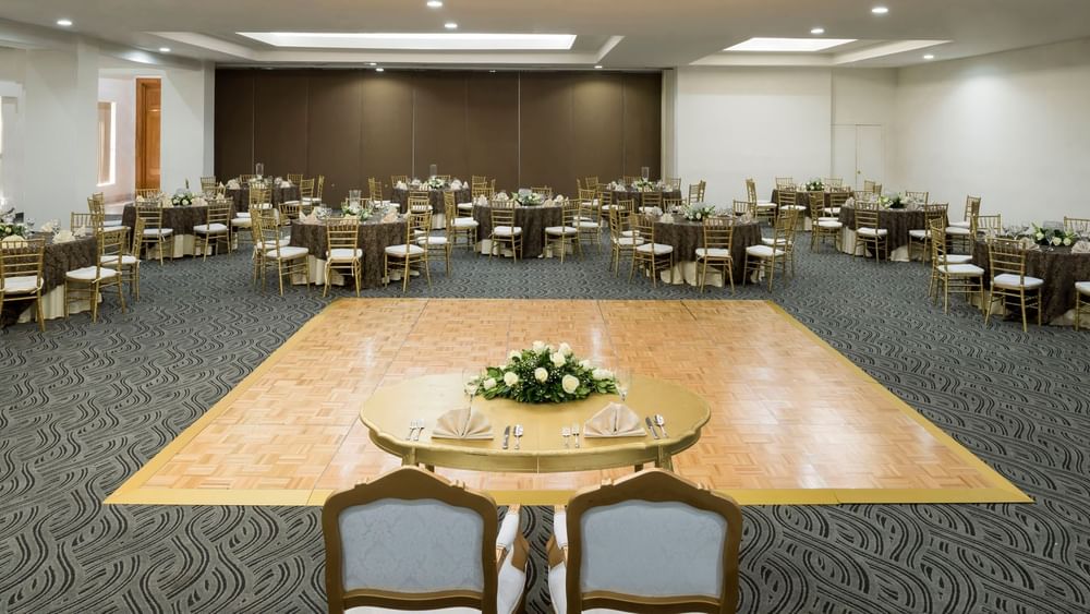 Gold chairs by round tables surrounding a wooden dance floor under a coffered ceiling in Frankfurt at Real Inn Mexicali