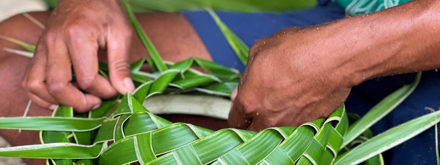 Artisan weaving a green palm leaf basket by a woven mat at The Naviti Resort in Korolevu, Fiji