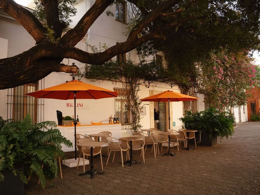 Outdoor Bistro Champan Bar with orange umbrellas, modern chairs, and lush greenery at Billini Hotel Historic Luxury