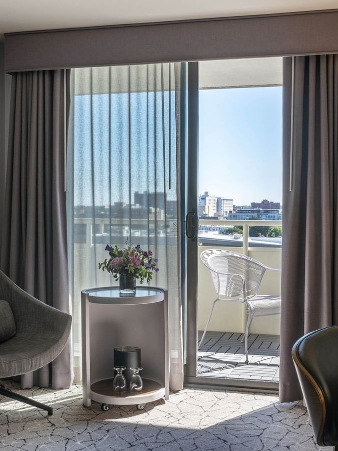 Gray swivel chair by a round table near a sunlit balcony under a tripod lamp in Premier Junior Suites at Warwick Denver
