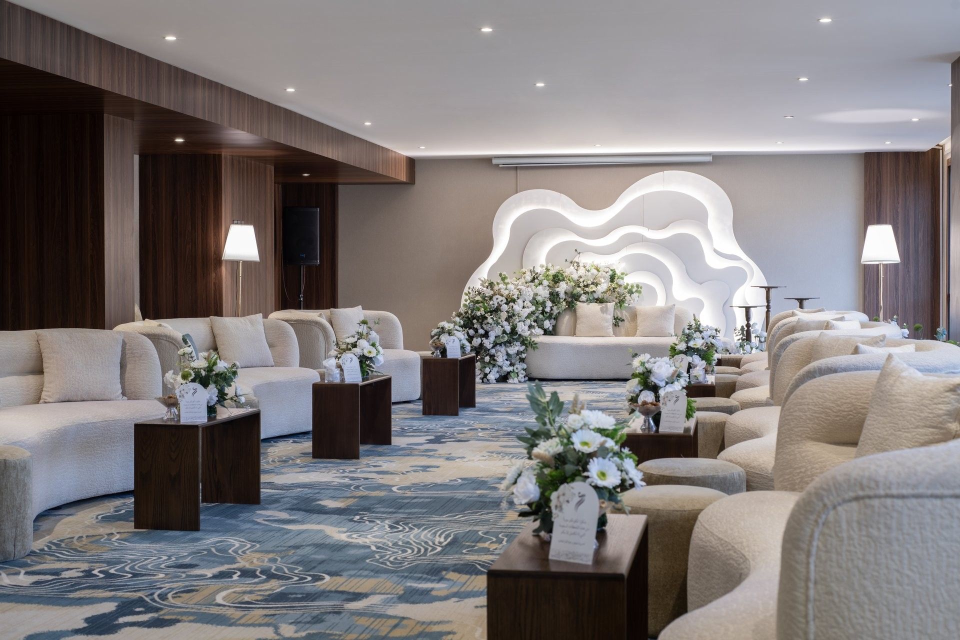 Cream sofas surrounding flower arrangements on a blue rug under bright lights in Amarige Hall at Warwick Hotels and Resorts
