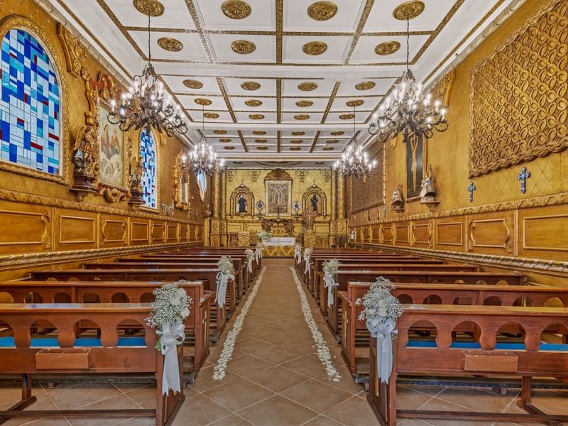 Beautifully decorated church or chapel near Fiesta Americana, with golden walls, ornate chandeliers, and pews