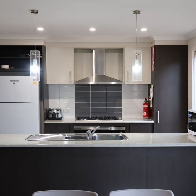 Modern kitchen with appliances, white countertops, and black cabinets at La Trobe University Regional Housing – Melton.