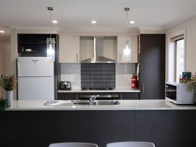 Modern kitchen with appliances, white countertops, and black cabinets at La Trobe University Regional Housing – Melton.