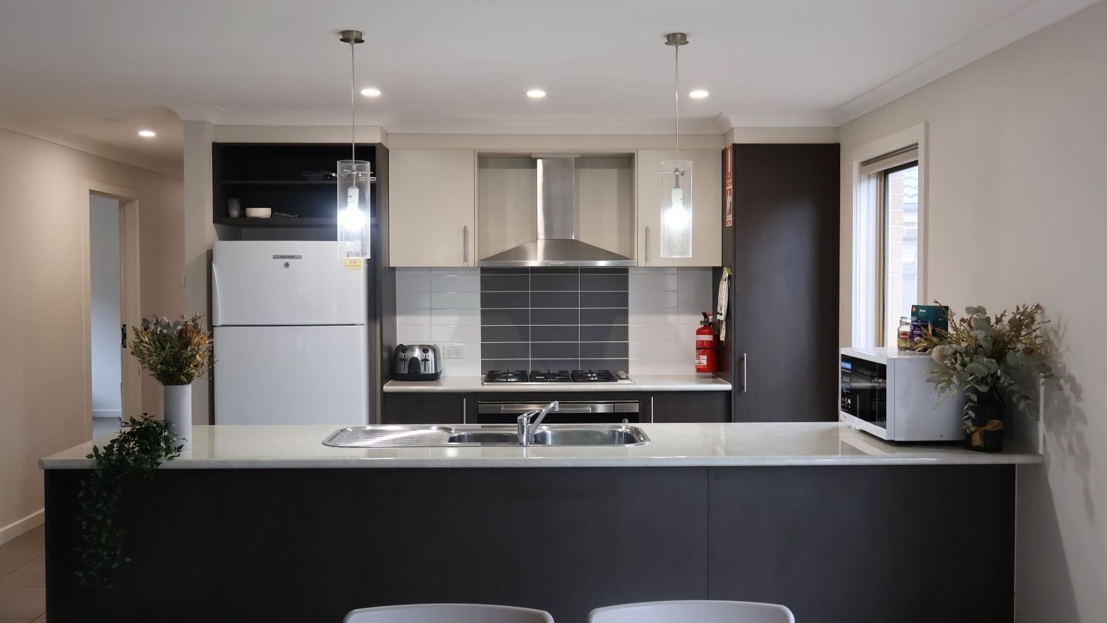 Modern kitchen with appliances, white countertops, and black cabinets at La Trobe University Regional Housing – Melton.