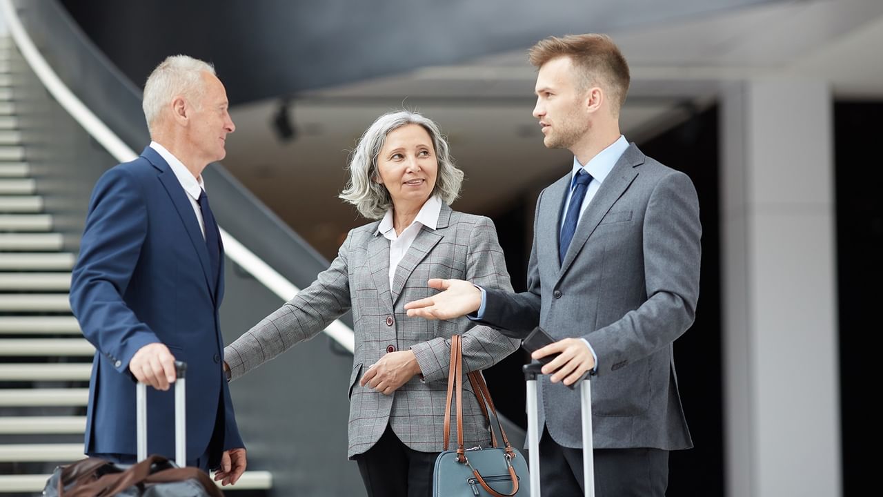 Three formally dressed travelers with luggage at an airport.