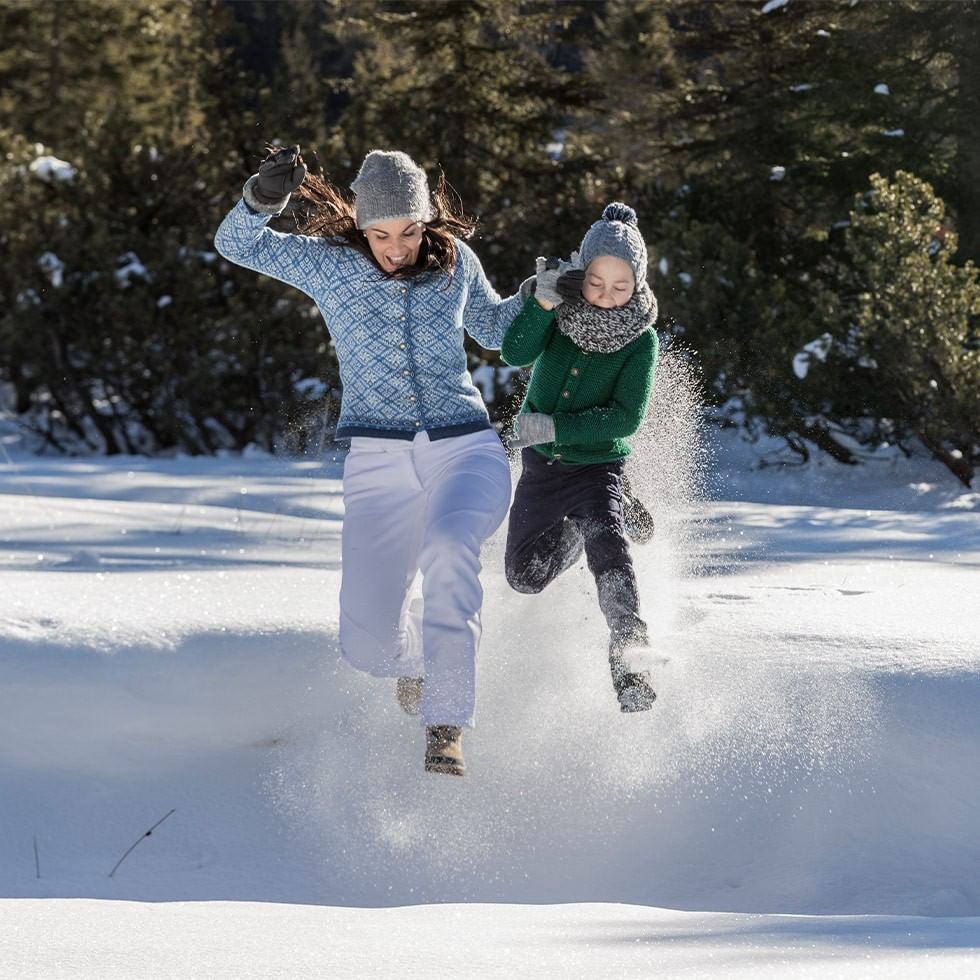 A woman and a child are running through snow, causing snow to spray around them.