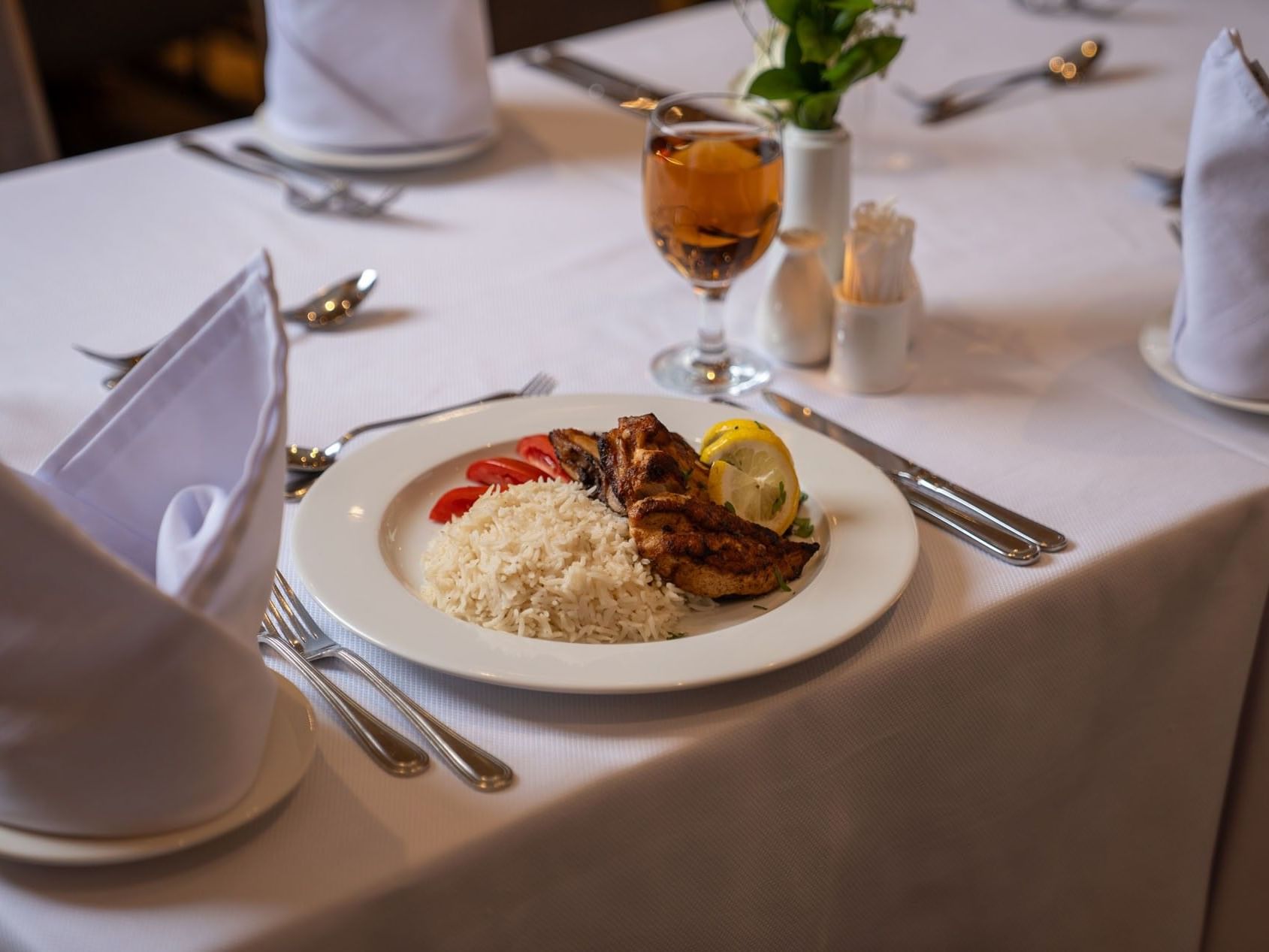 Plate of rice and chicken with lemon garnish and glass of wine at Saja by Warwick Madinah.