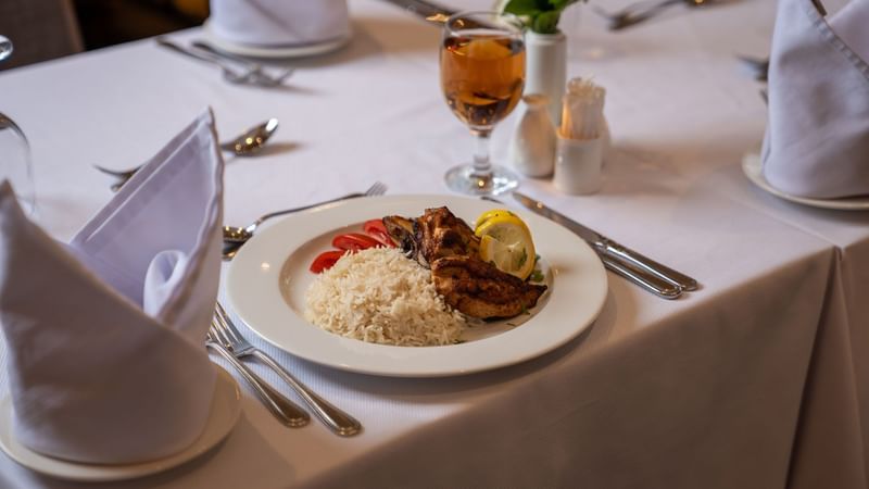 Plate of rice and chicken with lemon garnish and glass of wine at Saja by Warwick Madinah.