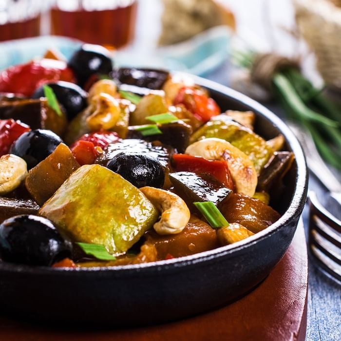 Schwarze Oliven und Gemüse in einer schwarzen Schüssel auf einem Tisch mit anderen Gerichten und Besteck.