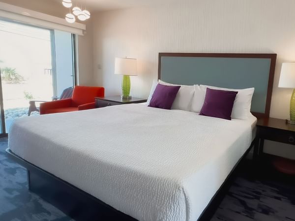 Guest room with king bed, lamps, patio doors, red chair