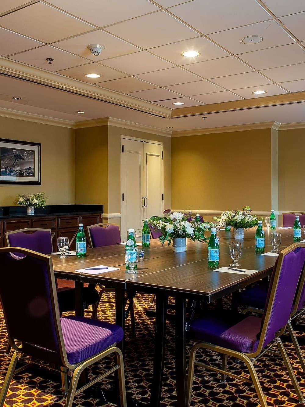 Long wooden table with purple chairs and water bottles under warm ceiling lights in Evans at Warwick Denver