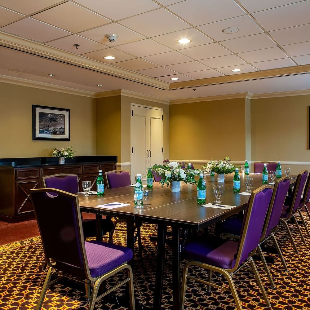 Long wooden table with purple chairs and water bottles under warm ceiling lights in Evans at Warwick Denver