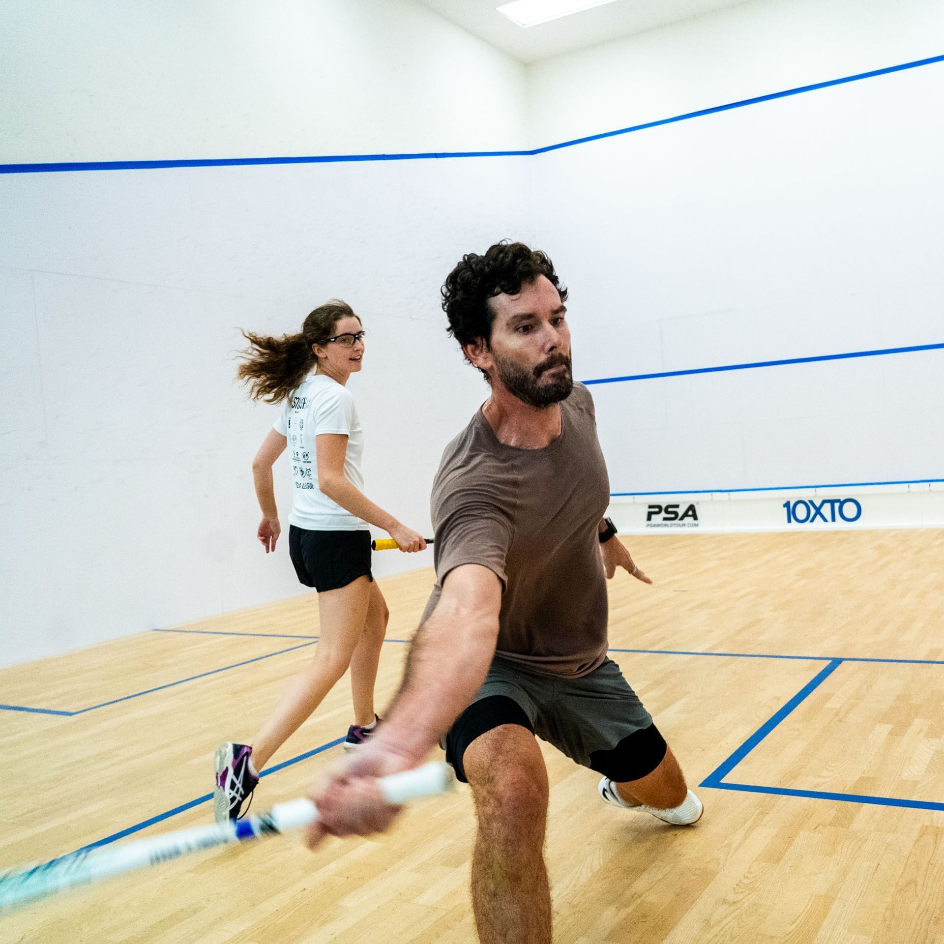 Man and woman playing squash on an indoor court with wooden flooring at 10XTO in Hotel X Toronto