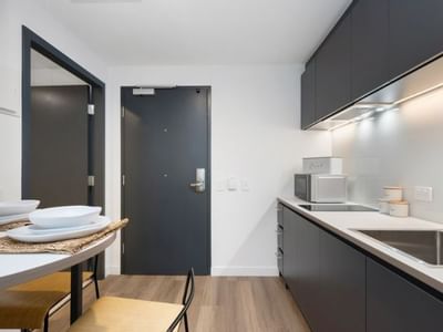 Modern kitchen with black cabinets, white counters, sink, microwave, and dining area with wooden table and chairs.