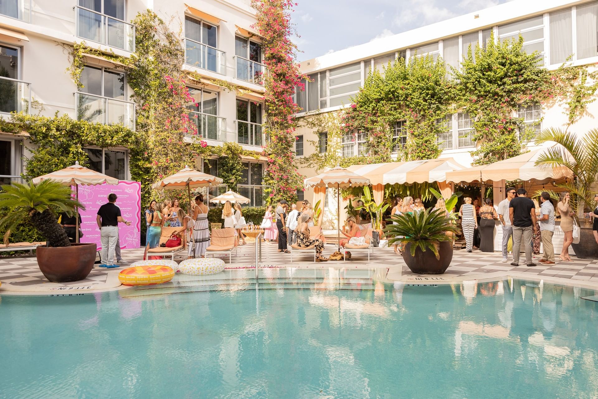 A group of people gathered around a pool with umbrellas and plants