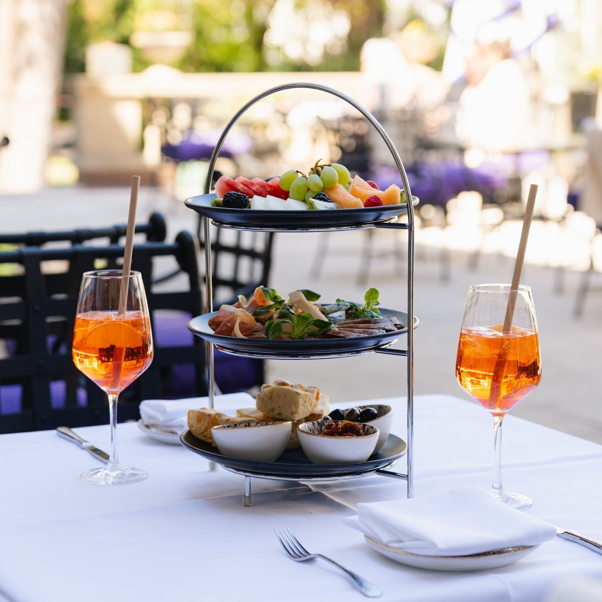 Two glasses of aperitivo and a tiered platter with assorted snacks and fruit.