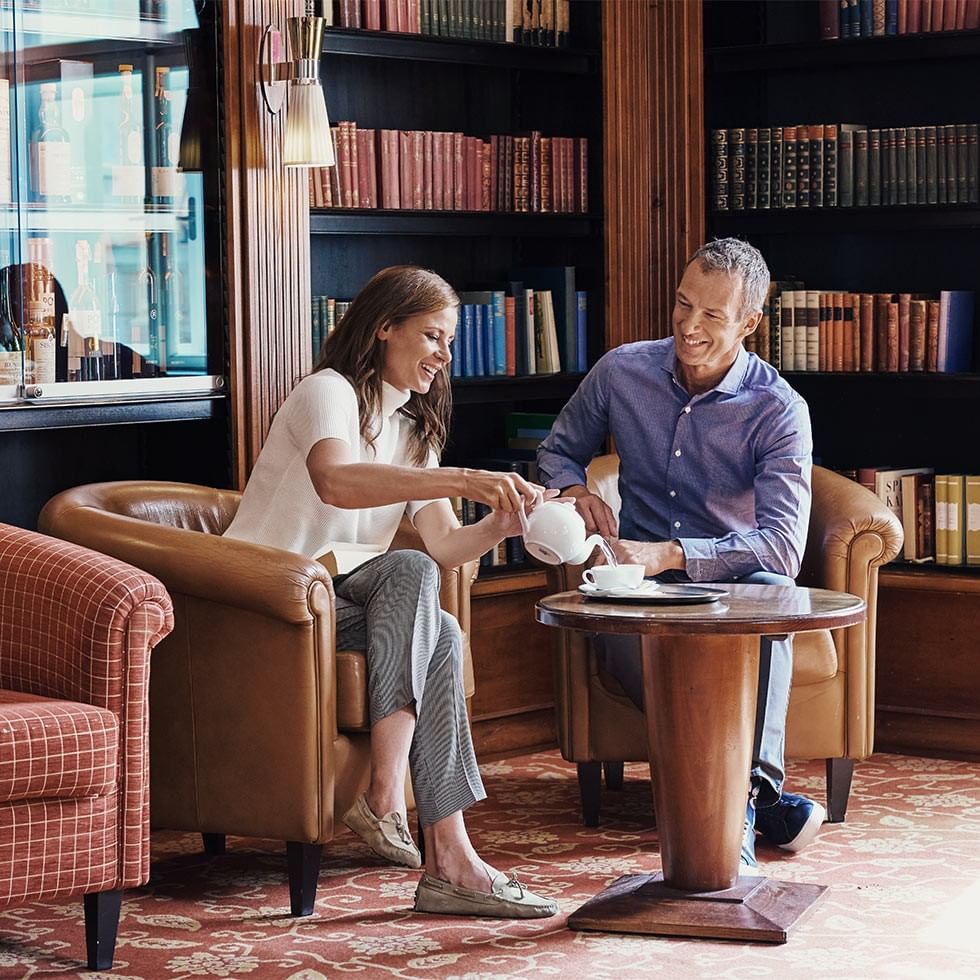 Frau und Mann lächelnd und Tee trinkend in einem Raum voller Bücher.