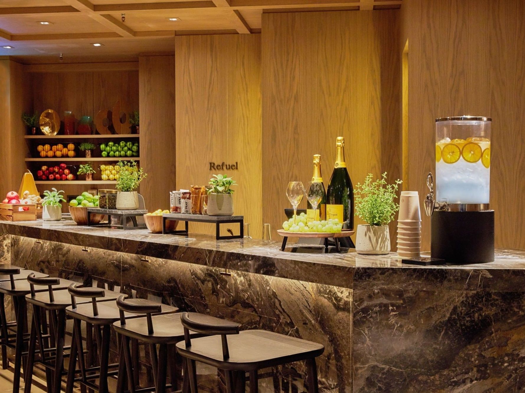 Refuel Bar with marble counter, black stools, and beverage displays at The Londoner Hotel