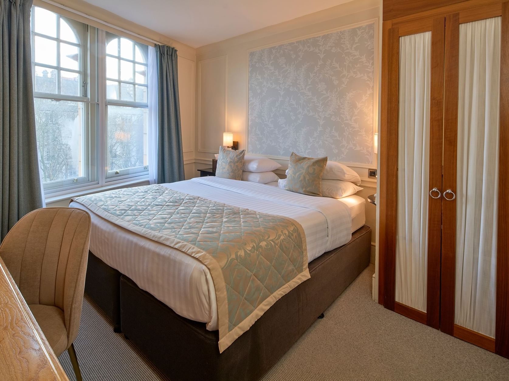 Standard double room with large windows, patterned wallpaper, wooden desk and fitted wardrobes at Sloane Square Hotel