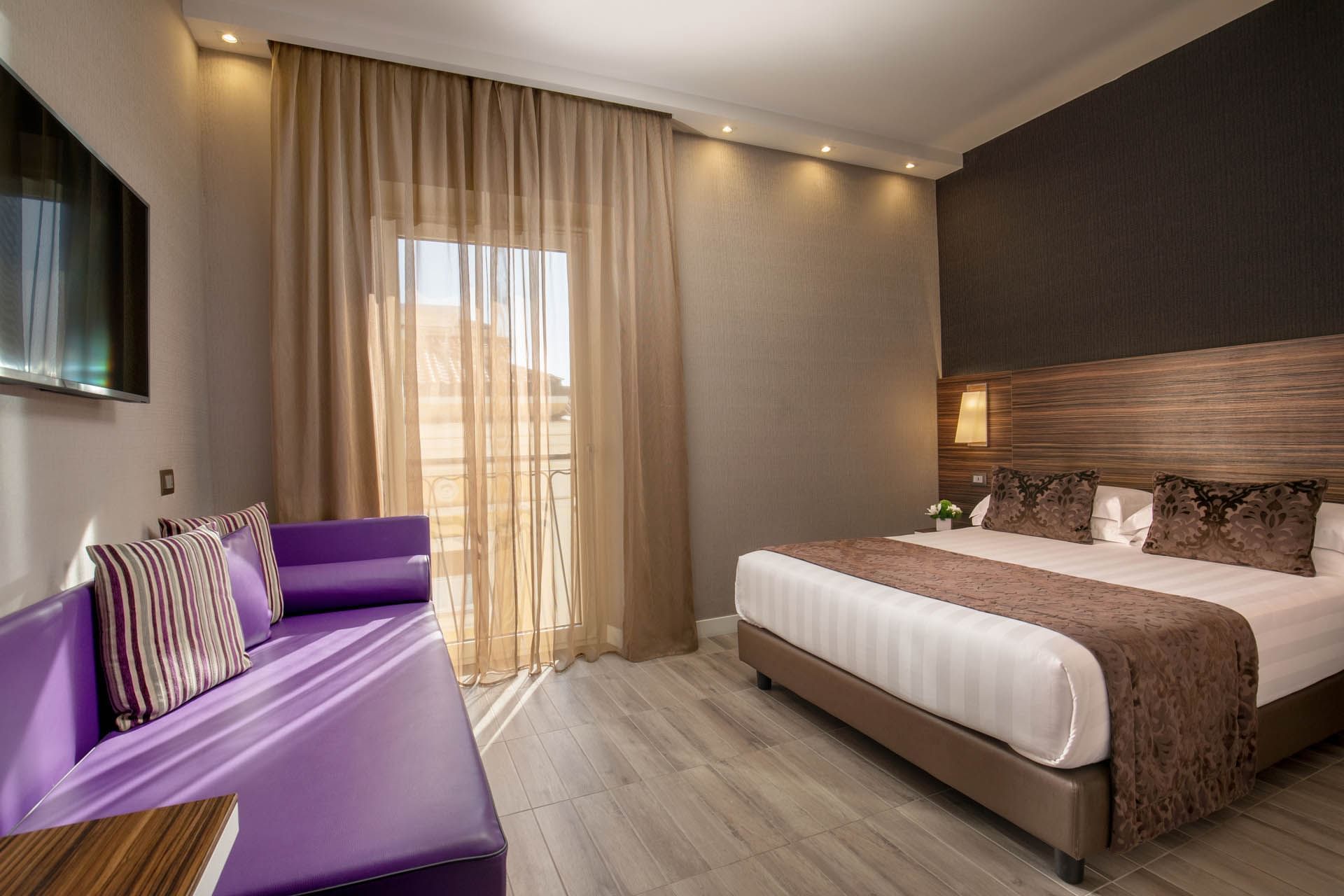 Family Room featuring a double bed, purple couch, large window with sheer curtains, and warm lighting at The Republic Hotel