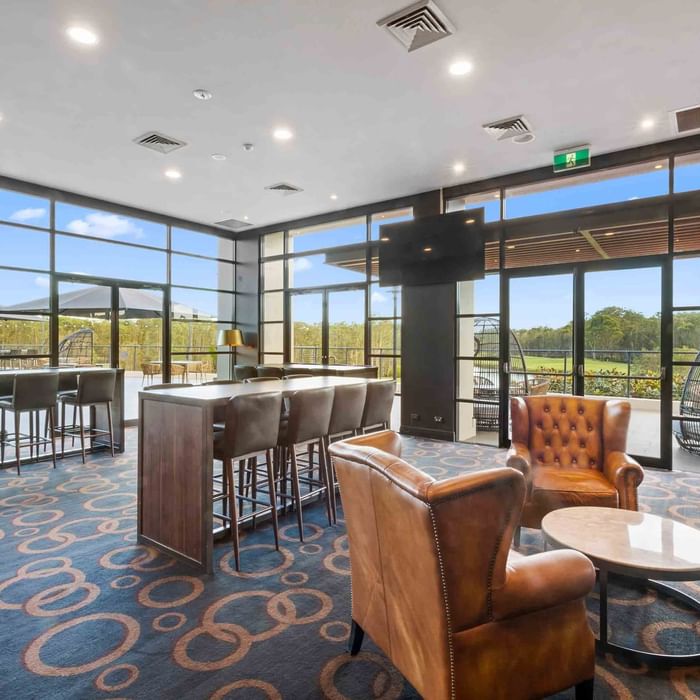 Wine Bar with stools, leather chairs, and large windows overlooking the golf course at Mercure Kooindah Waters