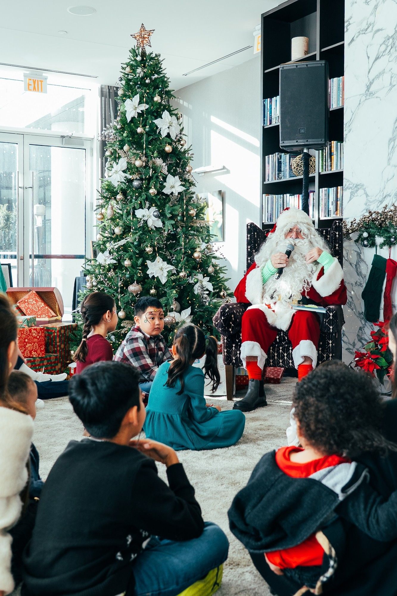Santa speaking to seated children by a decorated Christmas tree and wrapped gifts during holidays at Hotel X Toronto