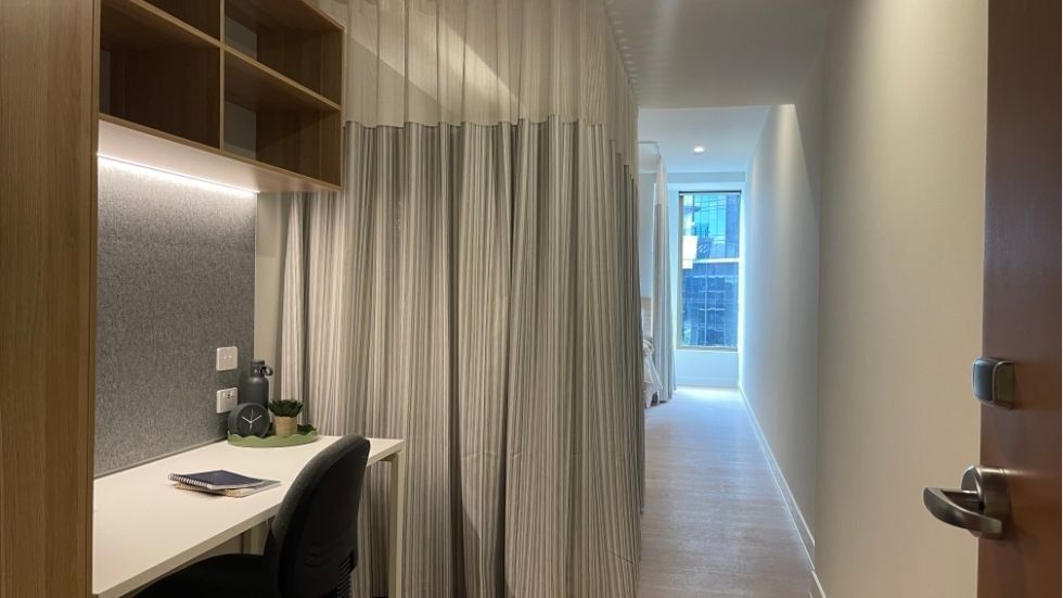 Modern room with desk, chair, curtained divider, and bright hallway within a 4 Bedroom Twin Share Apartment at UniLodge Brisbane City.