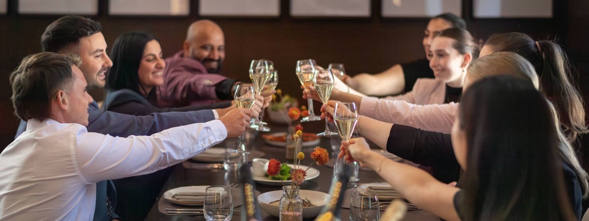 Group of diners raising champagne glasses in a toast at an elegant restaurant table for Bledisloe Cup Dining