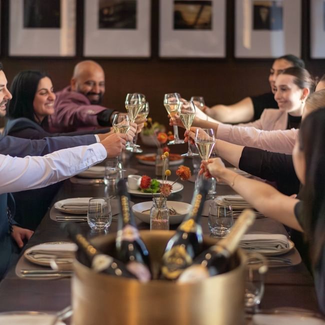 Group of diners raising champagne glasses in a toast at an elegant restaurant table for Bledisloe Cup Dining