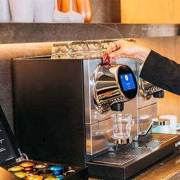 A hand inserting a coffee capsule into a modern espresso machine at The Terraces Resort & Spa