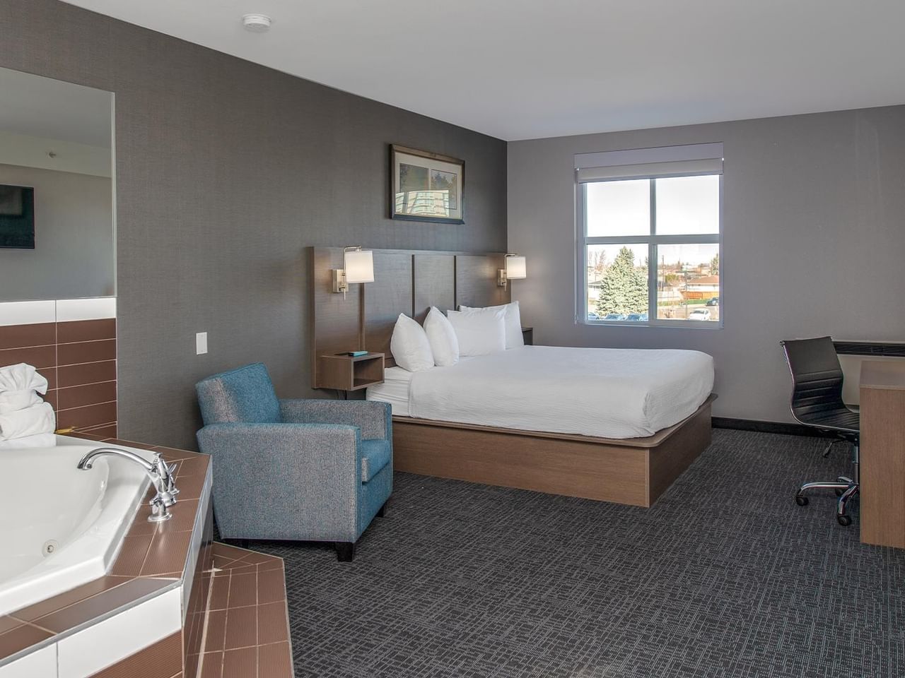 Room with bed, jetted tub, desk, and chair.