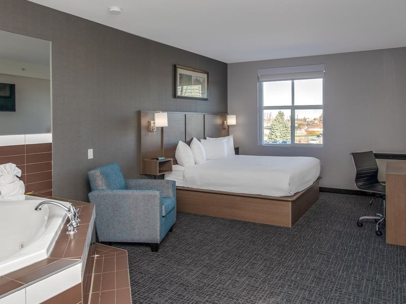 Room with bed, jetted tub, desk, and chair.