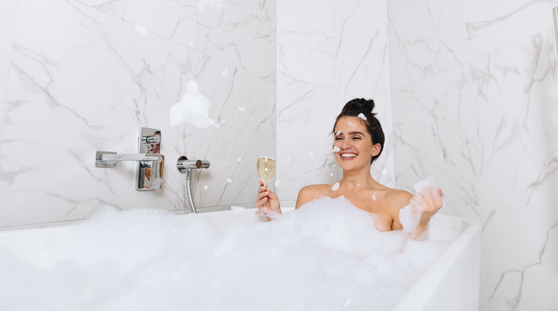 Lady enjoying champagne in a bubble bath at Pullman Melbourne CDB