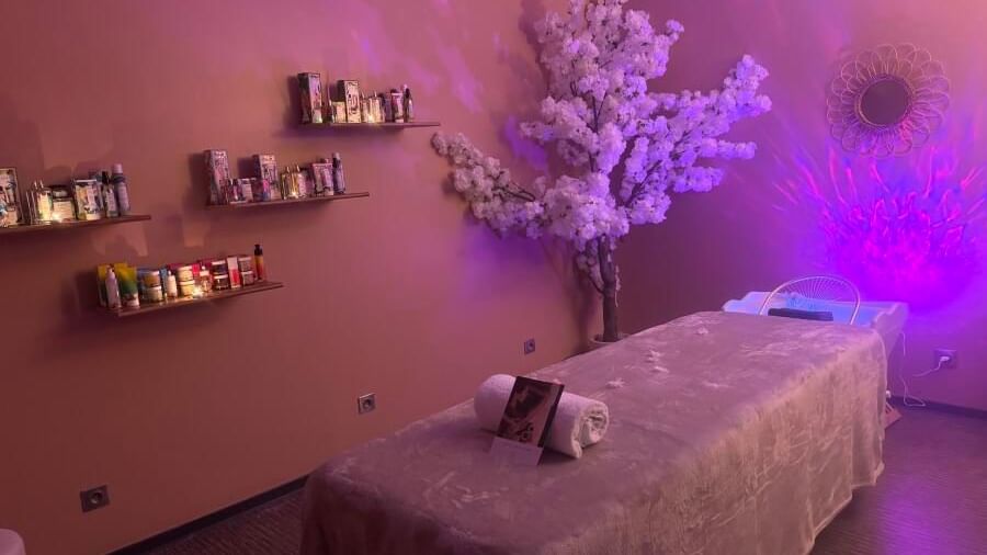 Chambre de soins avec lit, arbre floral, étagères de produits et éclairage violet sur les murs.