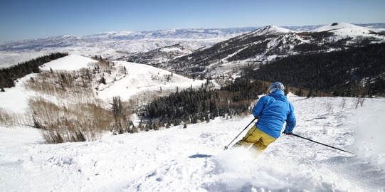 A man skiing downhill with mountain backdrop near The Chateaux Deer Valley