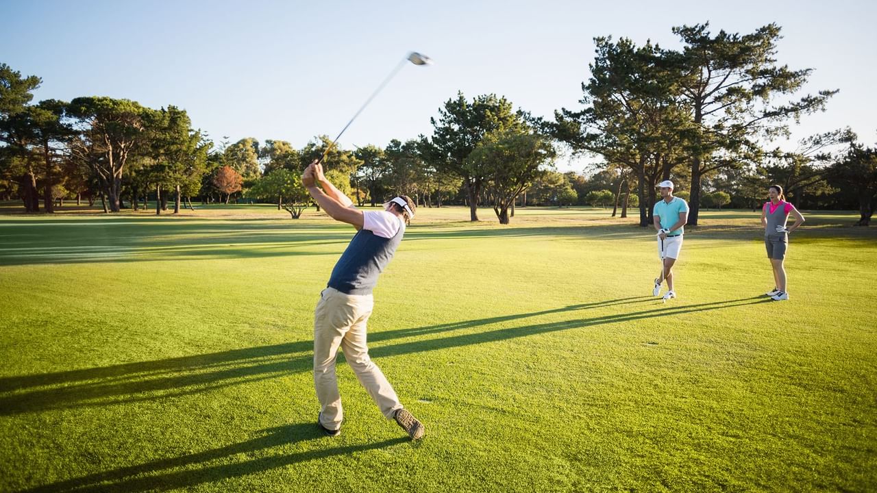 Golfer swinging a club on the golf course with another golfer watching nearby, near Coast Penticton Hotel