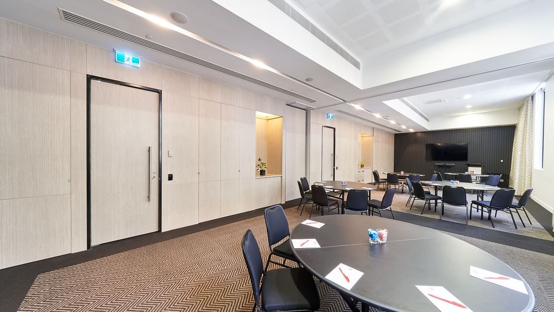 Round tables set up with chairs facing a large projection screen in The Think Tank at Ibis Adelaide