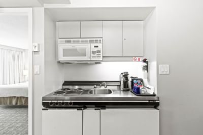 Compact kitchenette with stove, sink, microwave, & coffee station in a suite at Rosedale on Robson, hotel suites in Vancouver