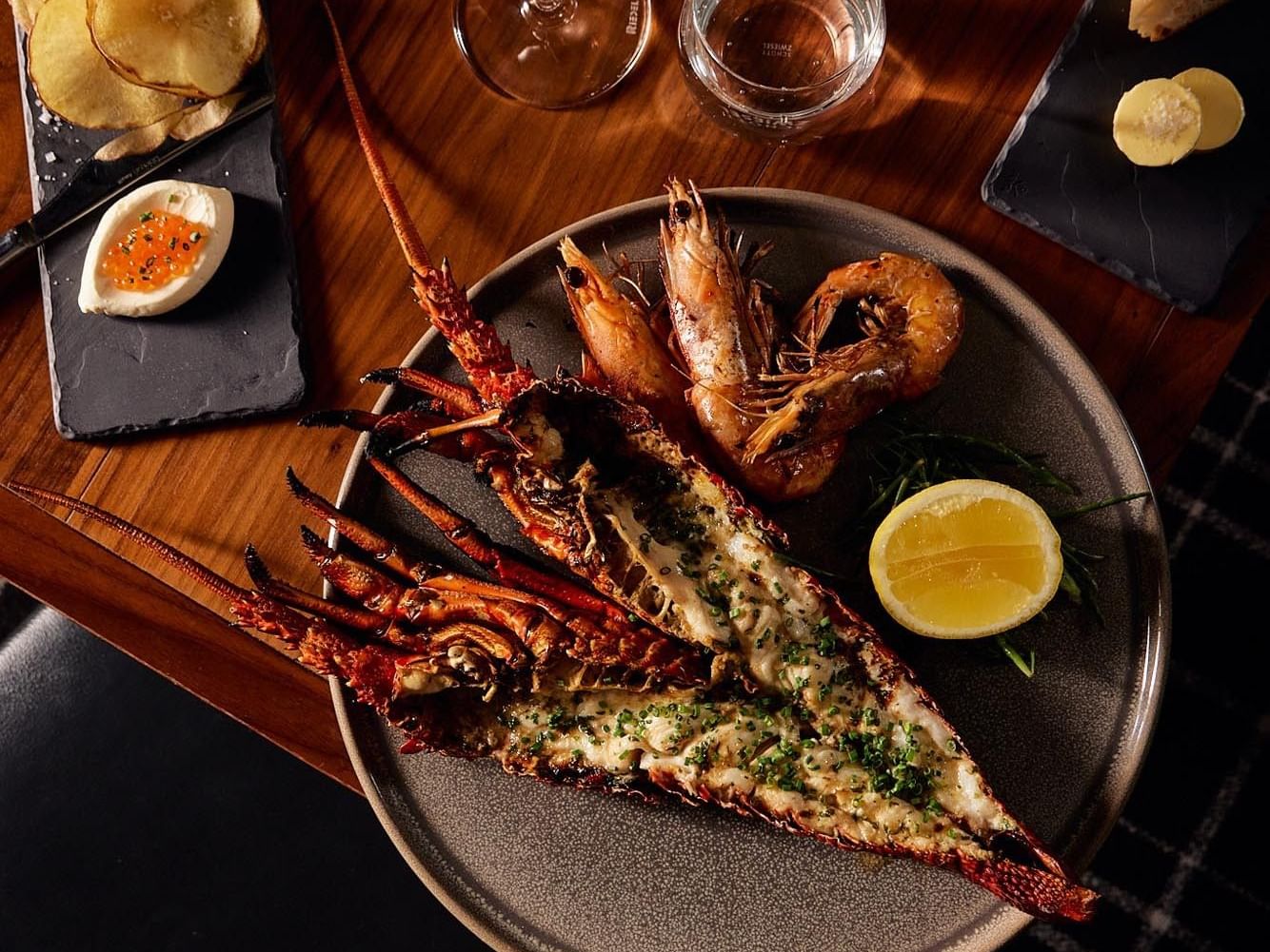Grilled rock lobster tail with herbs, served with king prawns & a lemon wedge in Coal Cellar + Grill at Amora Hotel Adelaide