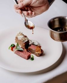 Server drizzling rich sauce over a plated steak dish with layered potato in The Capital Bar at Tom Brown at The Capital