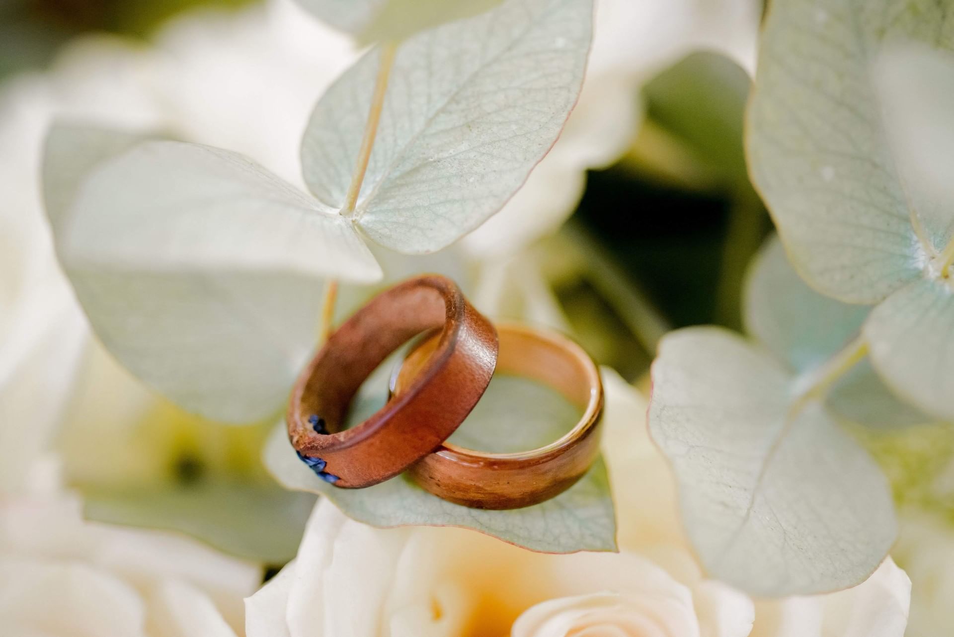 Close-up of wooden wedding rings resting on delicate white flowers at Cala Luna Boutique Hotel
