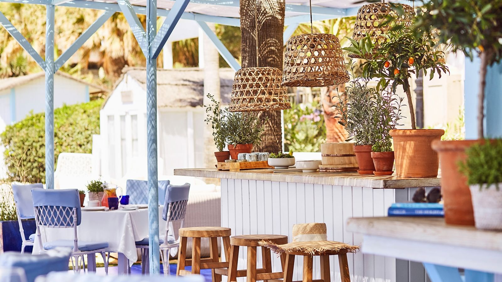 Beach bar with wooden bar stools and potted orange trees placed under woven light fixtures at Marbella Club