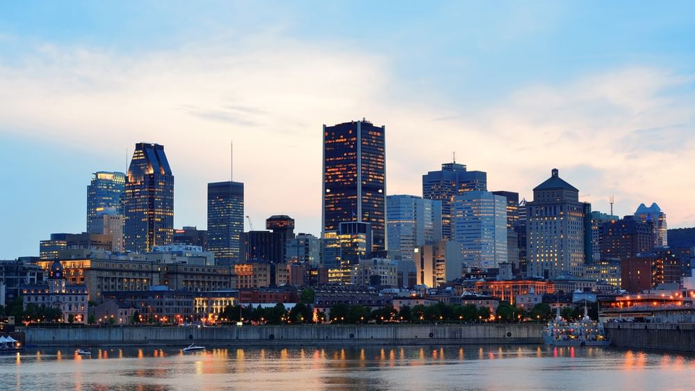 Paysage urbain de Montréal au crépuscule, avec des bâtiments illuminés et une vue sur le bord-de-mer.